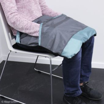 Frau sitzt auf Stuhl; auf ihre Beine ist eine Bein-Kugeldecke aufgelegt